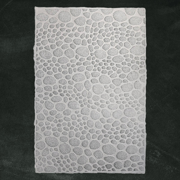 Intricate handmade paper from Kozo Studio showing lace-like stone patterns, made from mulberry fibers using water displacement for a translucent finish.