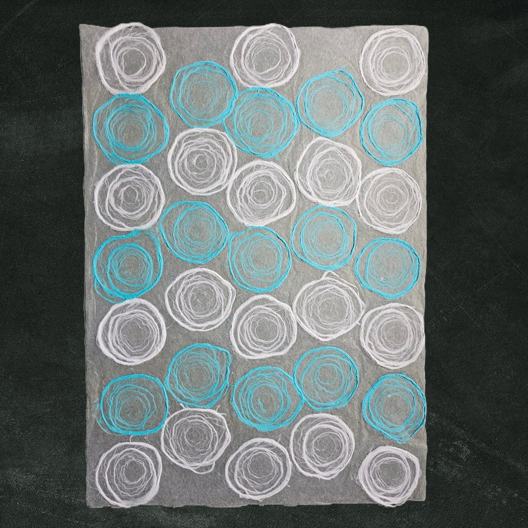 Close-up of artistic kozo studio paper design showing hand-drawn pulp circles on light blue and white mulberry paper, a unique handmade paper for crafts.
