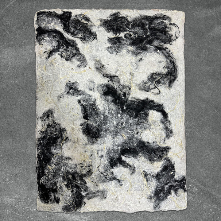 Unique handmade paper by Kozo Studio with a coarse surface and organic black and white tones made from premium mulberry fibers.