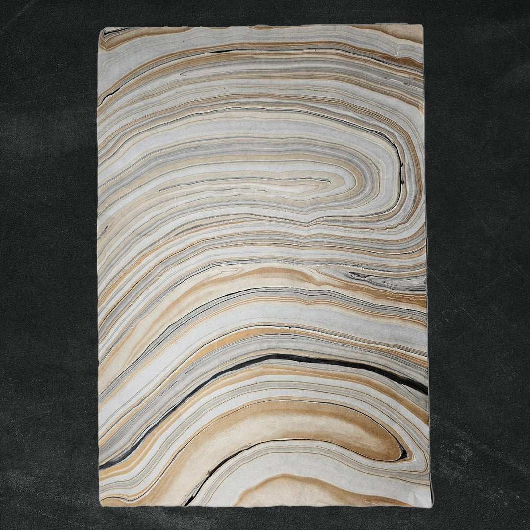 Textured mulberry paper from Kozo Studio with curled corner revealing layered marble design in gray and brown tones, ideal for handmade paper crafts and decorative use.