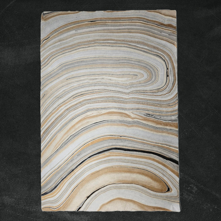 Textured mulberry paper from Kozo Studio with curled corner revealing layered marble design in gray and brown tones, ideal for handmade paper crafts and decorative use.