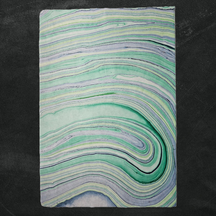 Detail of Kozo Studio's handmade paper with abstract marble design in vibrant blues and greens, created using traditional mulberry paper techniques.