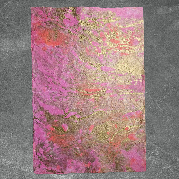 The Milano Kozo Paper - Design 4 by Kozo Studio features a textured mulberry sheet with gold and vibrant pink marbled patterns on a dark gray surface, blending in an organic, fluid design.