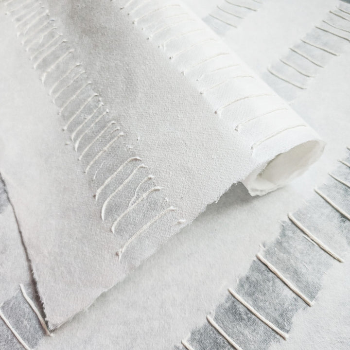 Close-up of handmade mulberry paper from Kozo Studio featuring a unique pulp rubbing texture with raised lines and elegant white stripes.