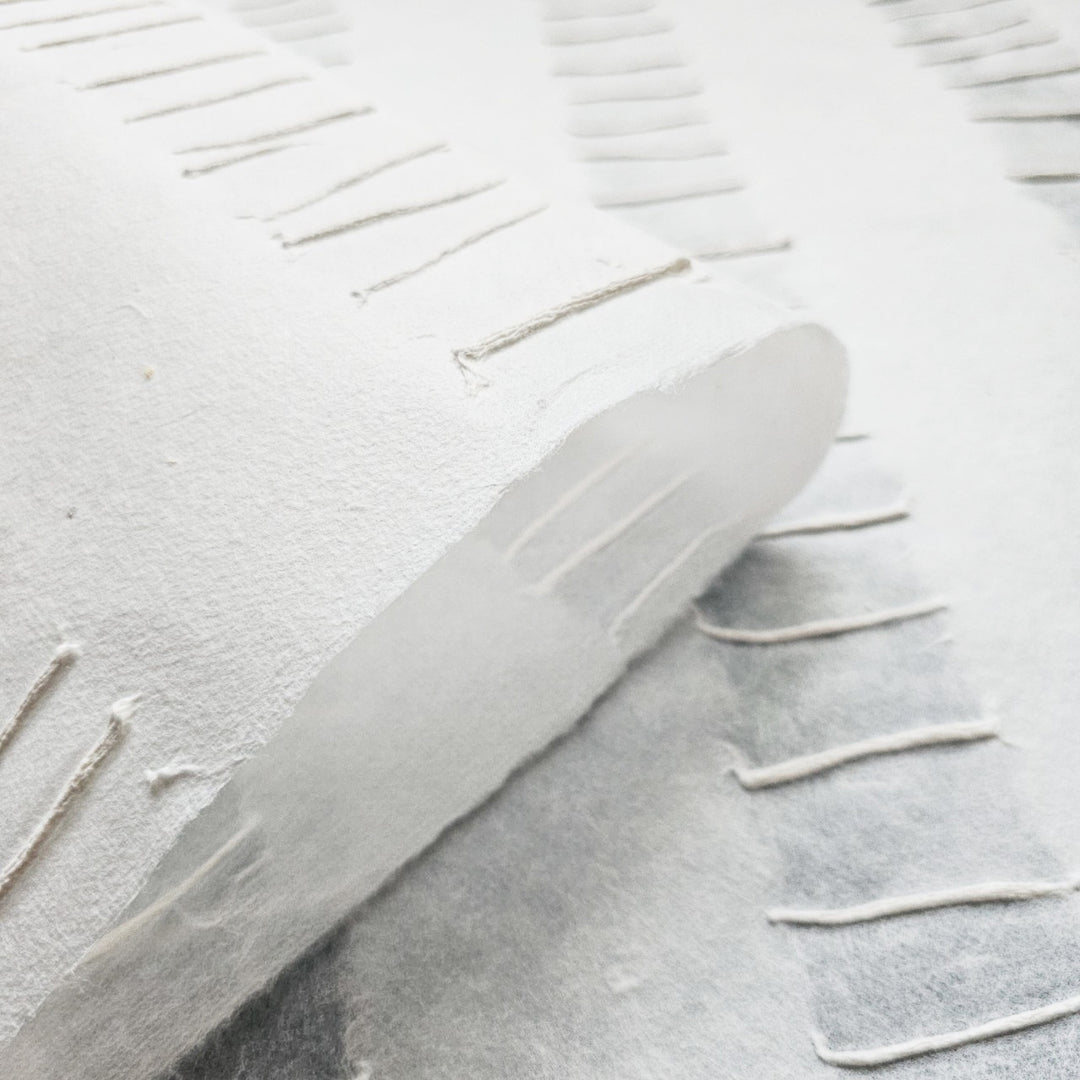The Handmade Fluo Kozo Paper (White) by Kozo Studio offers a close-up view of textured mulberry sheets with fringed edges, showcasing a handcrafted look. Visible fibers and a soft, matte finish add depth and subtle shadows to the layered sheets.