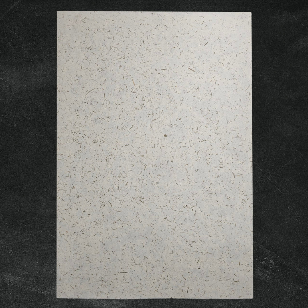 Eco-friendly handmade paper crafted by Kozo Studio, featuring bamboo confetti details on semi-translucent mulberry paper with natural brown and gray flecks.