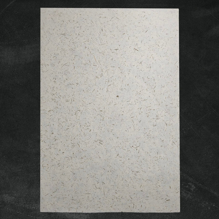 Eco-friendly handmade paper crafted by Kozo Studio, featuring bamboo confetti details on semi-translucent mulberry paper with natural brown and gray flecks.