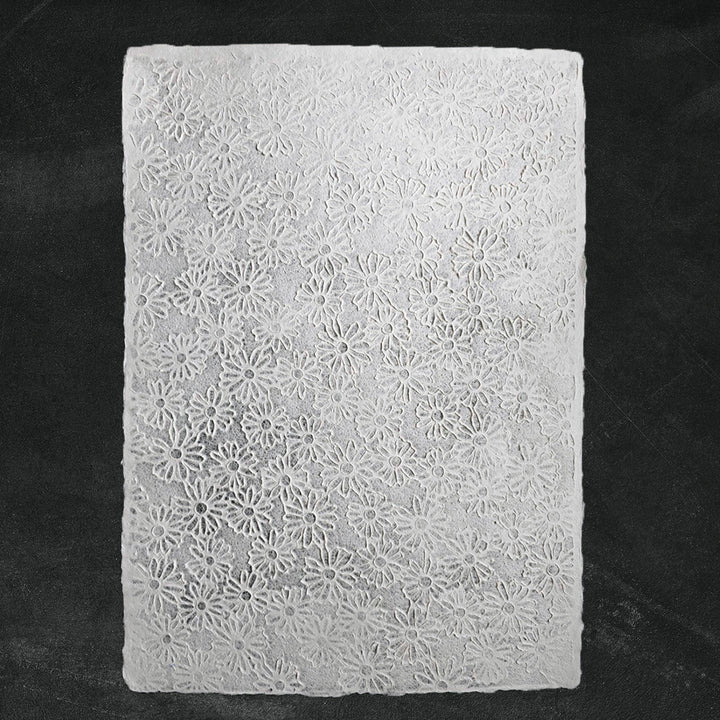 Close-up of handmade paper with intricate lace embossing and floral designs, crafted by Kozo Studio using traditional mulberry paper and Rakusui methods.