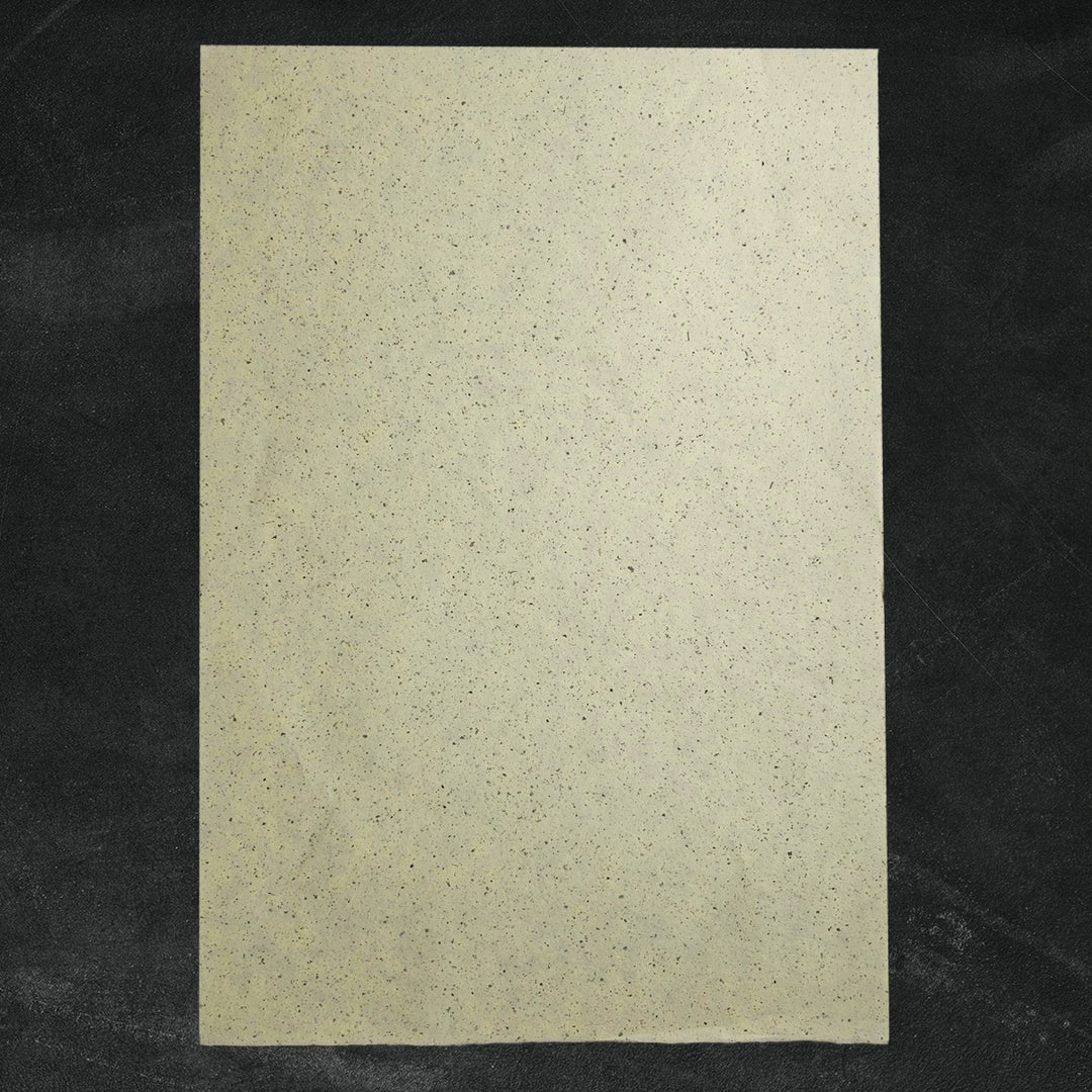 Textured mulberry paper by Kozo Studio, showing three semi-translucent handmade sheets with black and gray flecks from crushed kozo leaves arranged in gentle folds.