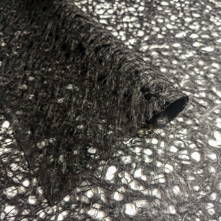 Close-up of Asarakusui Lace Paper (Black) by Kozo Studio, showcasing its textured netting of delicate mulberry paper, with intricate, irregular patterns and a lacy appearance. The partially unrolled lace paper reveals a sheer surface with various gaps and holes.