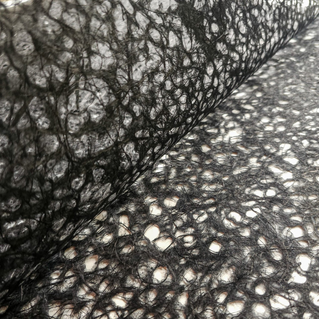A close-up of Asarakusui Lace Paper (Black) by Kozo Studio reveals its intricate openwork pattern, of delicate mulberry paper, with light filtering through the gaps, highlighting the detailed lace-like structure.