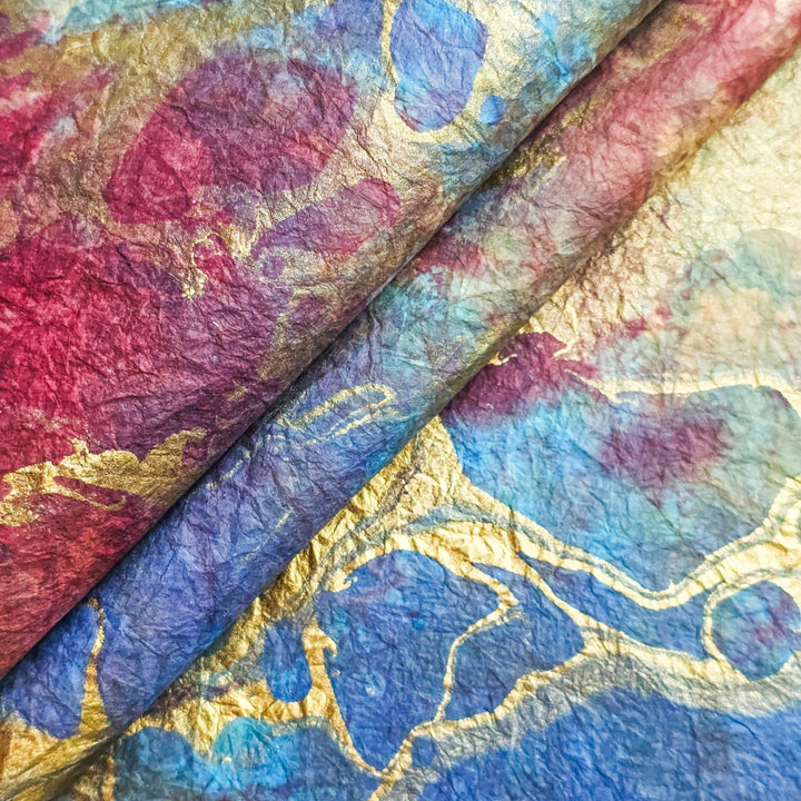 Close-up of handmade mulberry paper from Kozo Studio featuring Design 6, with swirling red, blue, and gold marbled patterns on a richly textured, crumpled surface.