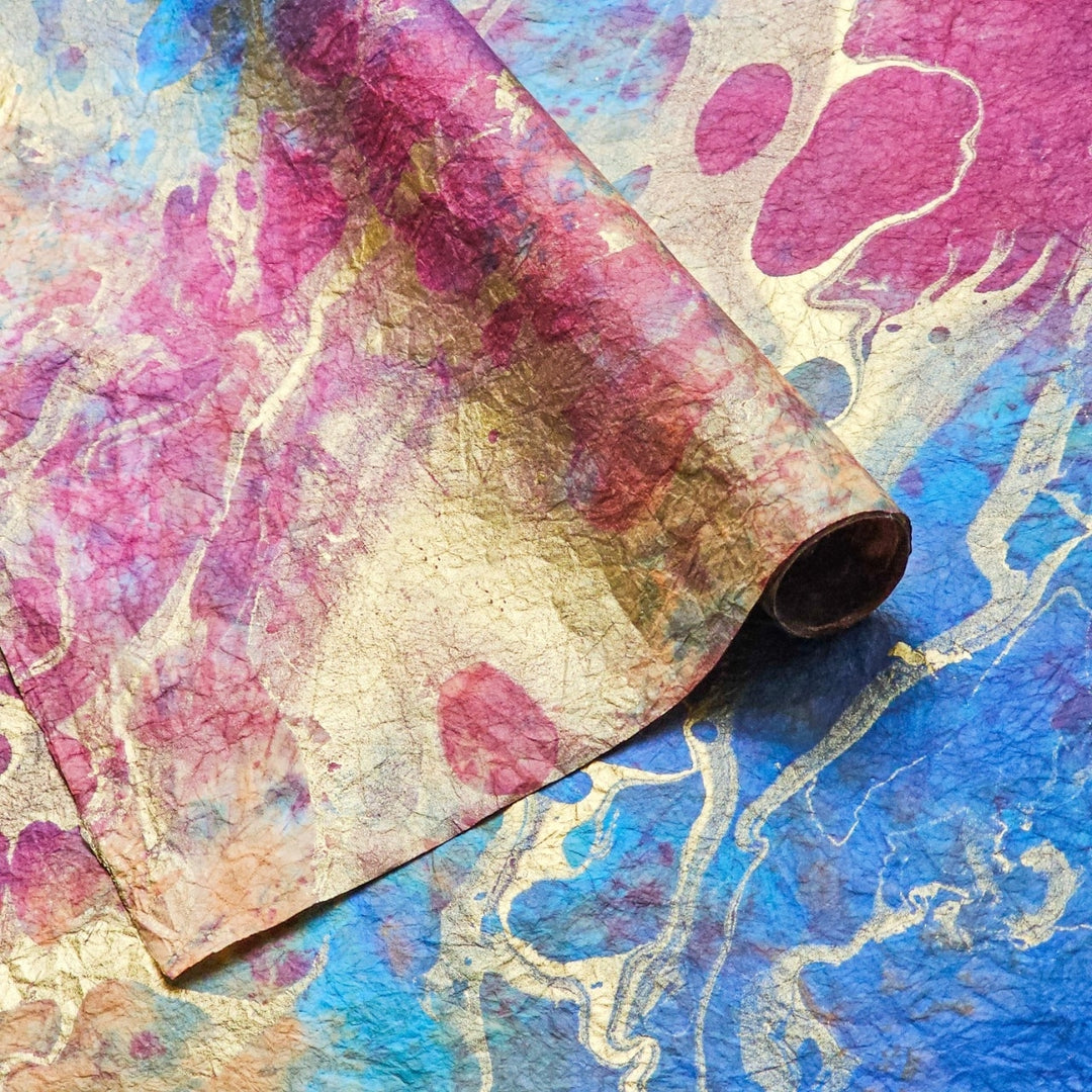 Abstract marbled design in red, blue, and gold on textured mulberry paper by Kozo Studio, highlighting the unique craftsmanship of handmade paper art.