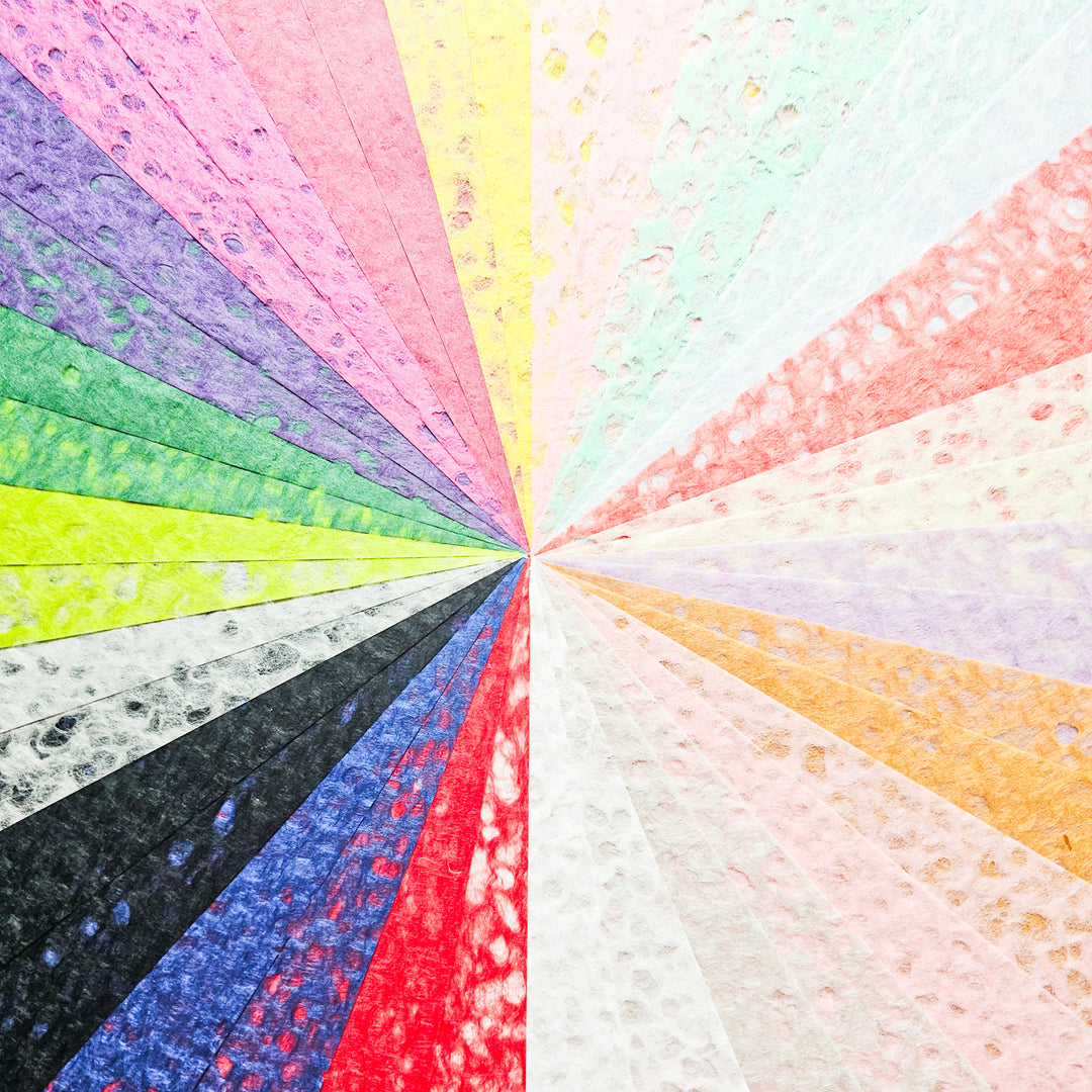 The Kozo Studio Assorted A4 Rakusui Mulberry Paper Set (40 Sheets) features vibrant, rainbow-colored sheets with a dotted textured finish, beautifully fanned out in a radial pattern for a striking display.
