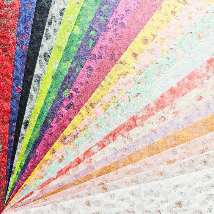 A fan-shaped spread of Kozo Studio’s Assorted A4 Rakusui Mulberry Paper Set (40 Sheets), each decorated with vibrant spots, extends from the bottom left corner toward the top and right edges.