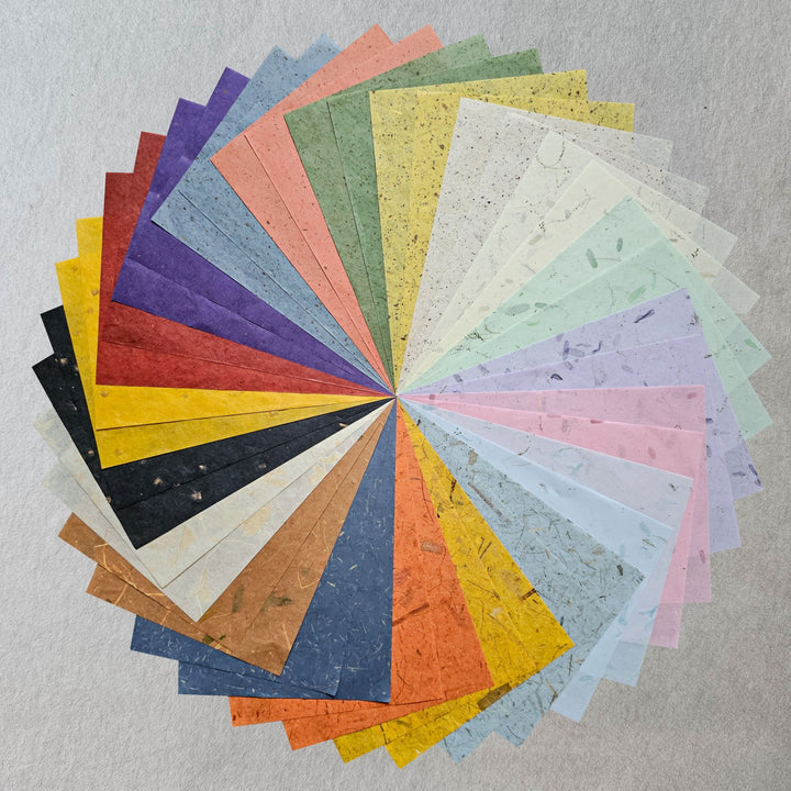 The Kozo Studio Assorted A4 Mix Leaf & Flower Mulberry Paper Set (40 Sheets) features vibrant, textured sheets in blue, green, yellow, pink, and more—ideal for DIY crafts—displayed fanned out on a neutral gray background.