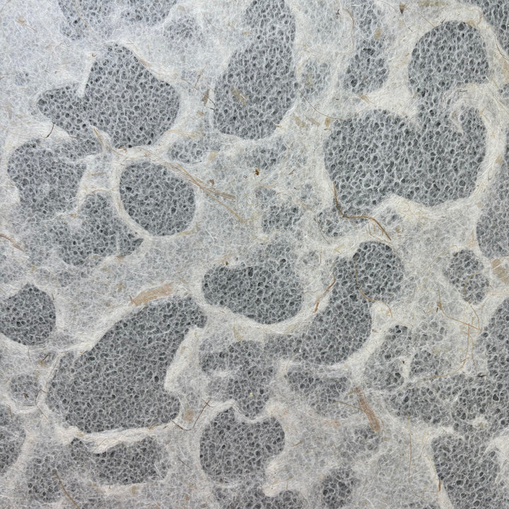 Close-up of Tidal Lace Kozo Paper (Banana Fiber) by Kozo Studio, showing irregular gray shapes on a light, fibrous background for an eco-friendly look with natural fibers and unique patterns.