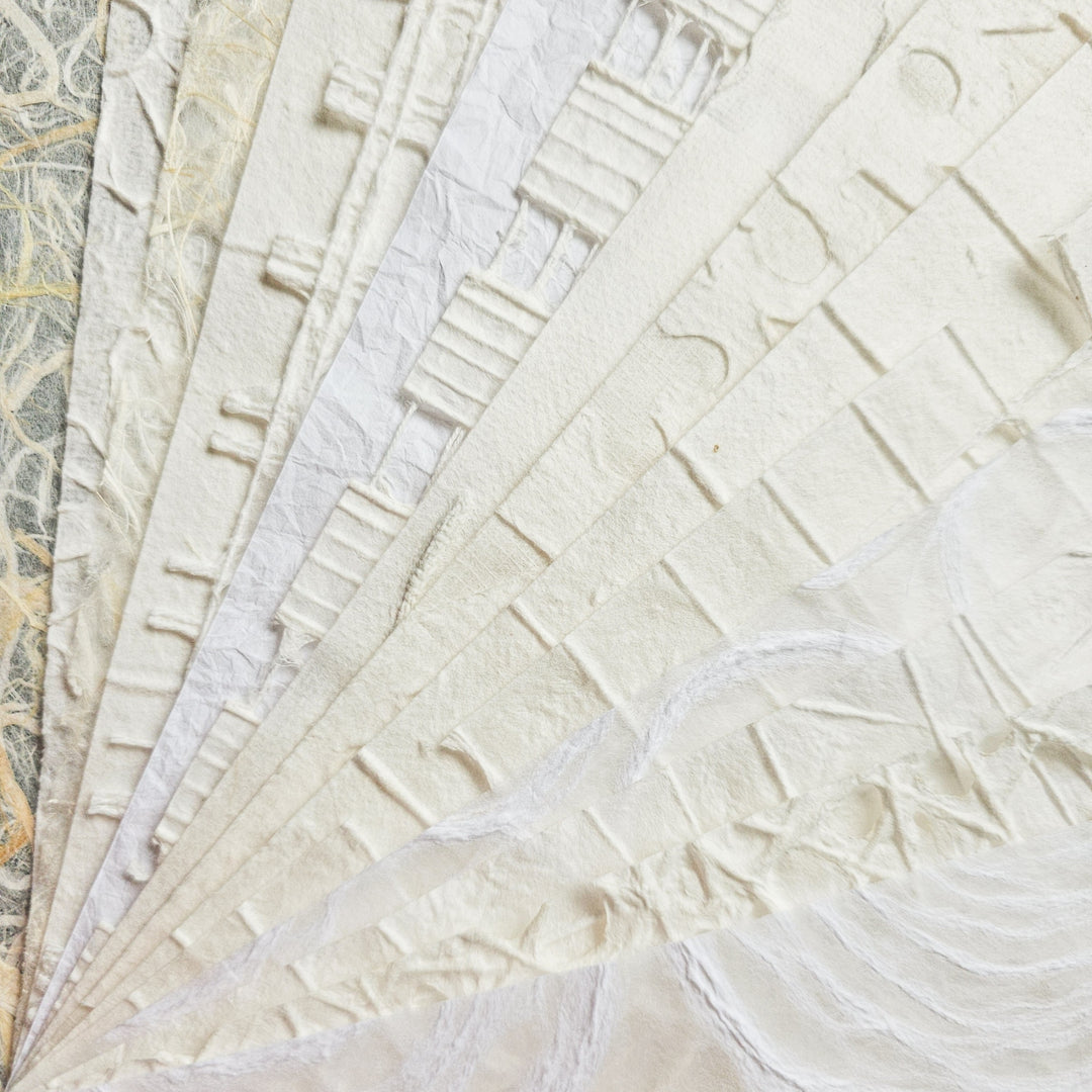 Close-up of the intricate design on Kozo Studios A4 Texture Treasure Kozo Paper Pack #1, showcasing overlapping sheets of mulberry paper with textured, embossed patterns. The mix of soft white and off-white hues is subtly enhanced by light, highlighting its delicate details.
