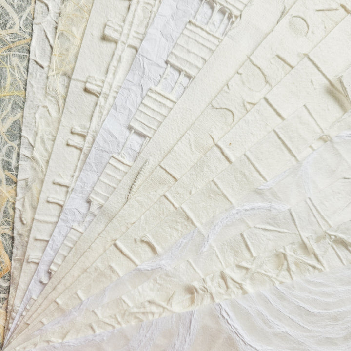 Close-up of the intricate design on Kozo Studios A4 Texture Treasure Kozo Paper Pack #1, showcasing overlapping sheets of mulberry paper with textured, embossed patterns. The mix of soft white and off-white hues is subtly enhanced by light, highlighting its delicate details.