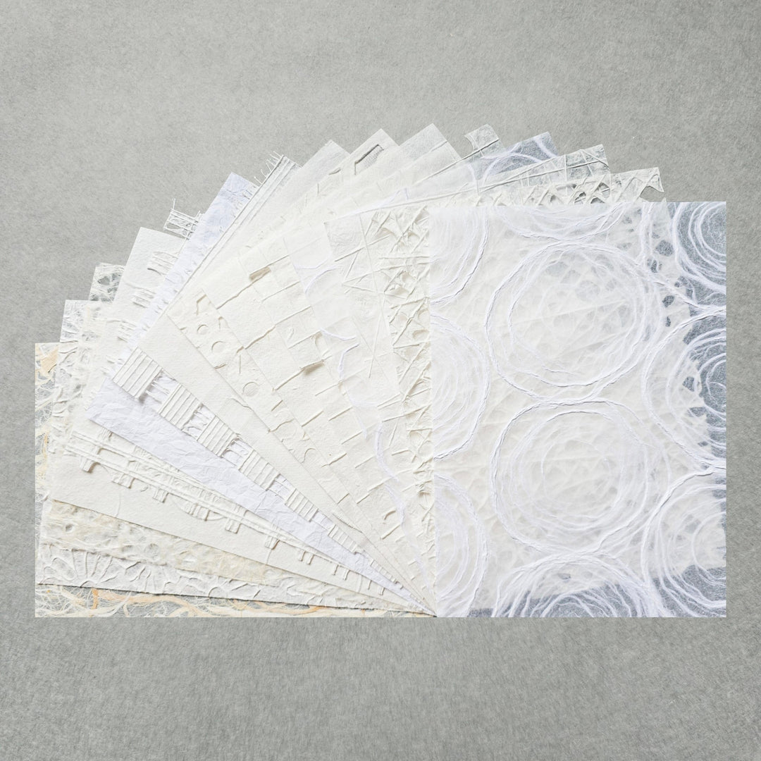 The A4 Texture Treasure Kozo Paper Pack #1 by Kozo Studio features textured white and light grey mulberry papers. Each sheet boasts unique patterns like circles, lines, and geometric shapes, creating a delicate and intricate display against a plain background.