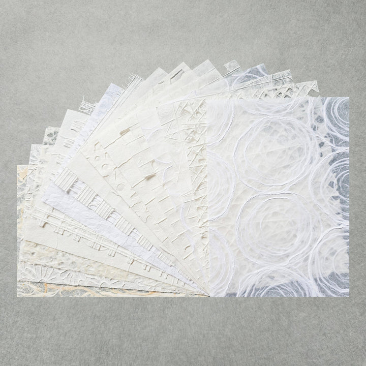 The A4 Texture Treasure Kozo Paper Pack #1 by Kozo Studio features textured white and light grey mulberry papers. Each sheet boasts unique patterns like circles, lines, and geometric shapes, creating a delicate and intricate display against a plain background.