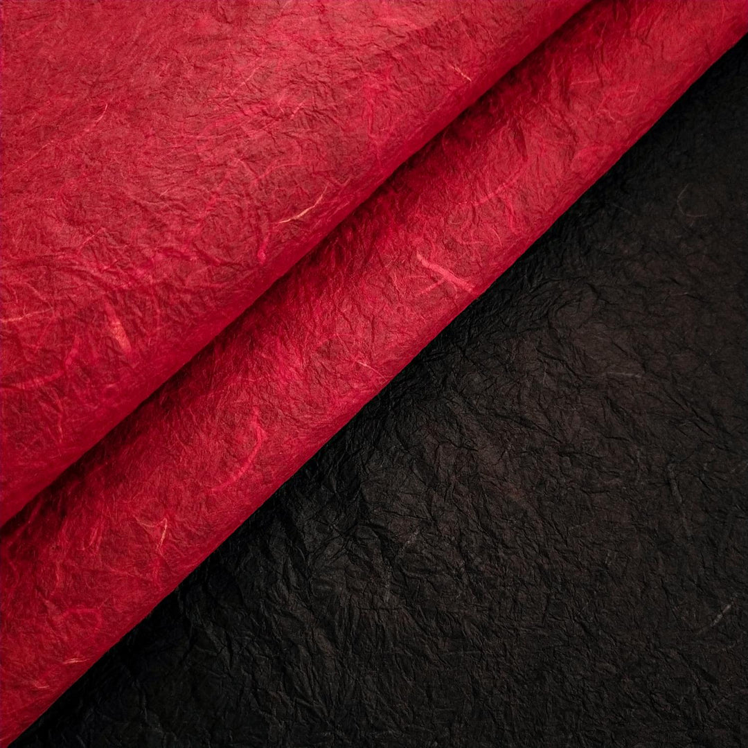 Photo of Kozo Studio's Momigami paper with red mulberry paper curled back to reveal black side, emphasizing the handmade double-sided craftsmanship.