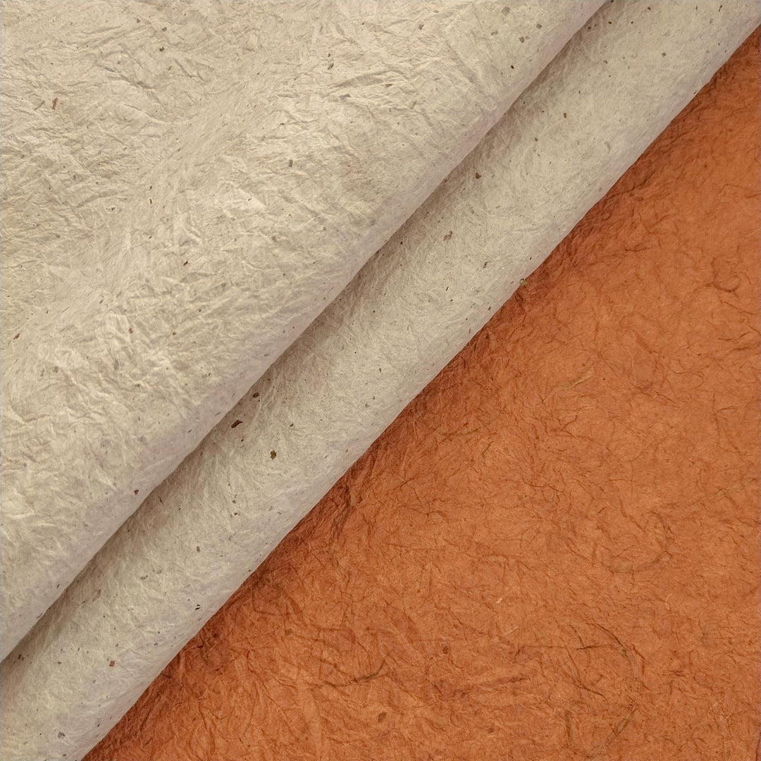 A piece of mulberry paper crafted by Kozo Studio is shown curling slightly on a flat surface, highlighting its hand-crinkled texture and dual tones.