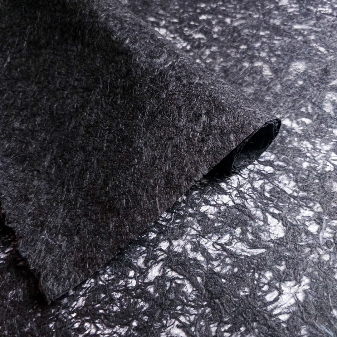 Close-up of black mulberry paper from Kozo Studio, showcasing its translucent handmade base with organic fiber strands, ideal for creative art and design projects.