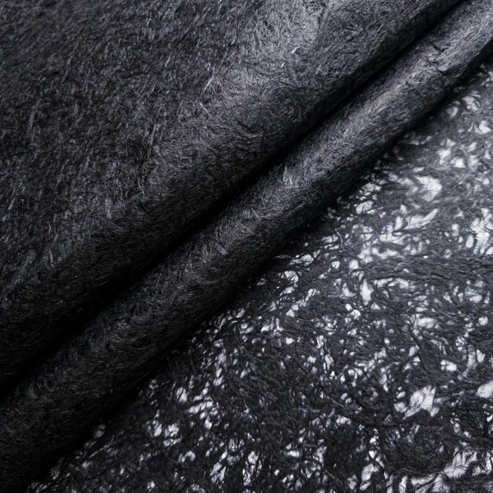 Close-up of Fiber Veil Kozo Paper (Black) by Kozo Studio, featuring a textured, fibrous mulberry surface. The top is soft and matte, while the bottom has a shinier finish with intricate patterns, creating a contrasting texture and sheen.