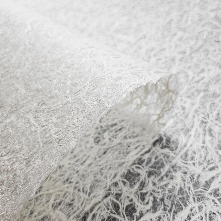 Close-up of Fiber Veil Kozo Paper (White) by Kozo Studio, showcasing its fibrous, lace-like texture against a blurred background of similar material. The mulberry papers surface is intricately detailed and slightly curved.