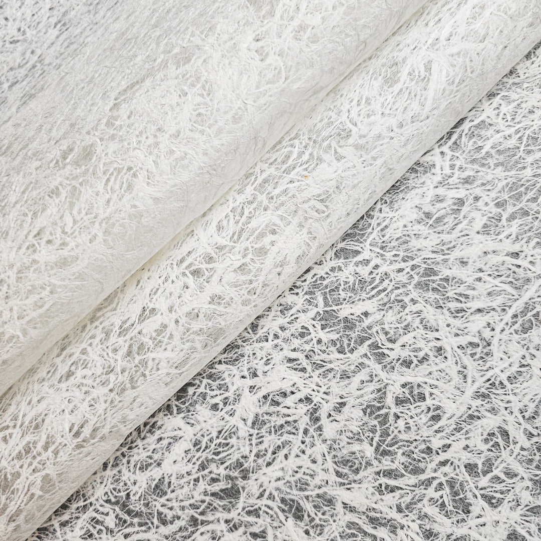 Close-up of Fiber Veil Kozo Paper (White) by Kozo Studio, featuring a textured, fibrous appearance with a delicate web-like pattern. This layered mulberry paper highlights intricate details and offers a slightly translucent quality.