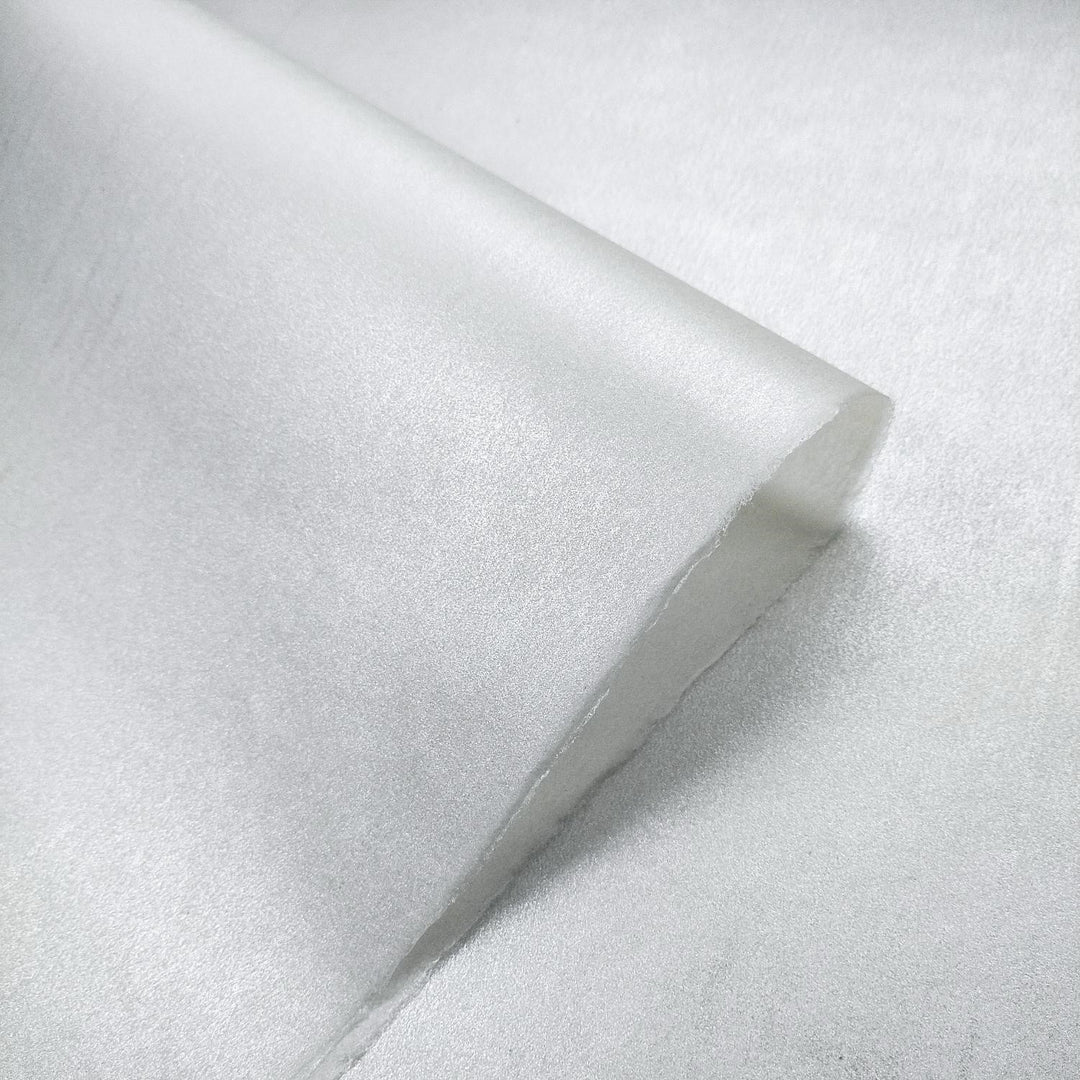 A roll of handmade paper from Kozo Studio unfurls to reveal shimmering metallic kozo fiber with subtle rice paper-style texture and curled edges.