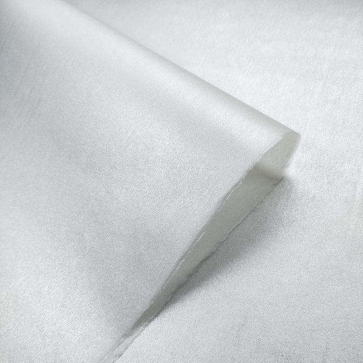 A roll of handmade paper from Kozo Studio unfurls to reveal shimmering metallic kozo fiber with subtle rice paper-style texture and curled edges.