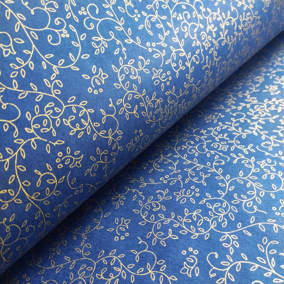 Kozo Studio handmade mulberry paper in a close-up showing gold floral tendrils on a smooth blue background with a folded sheet emphasizing the design continuity.