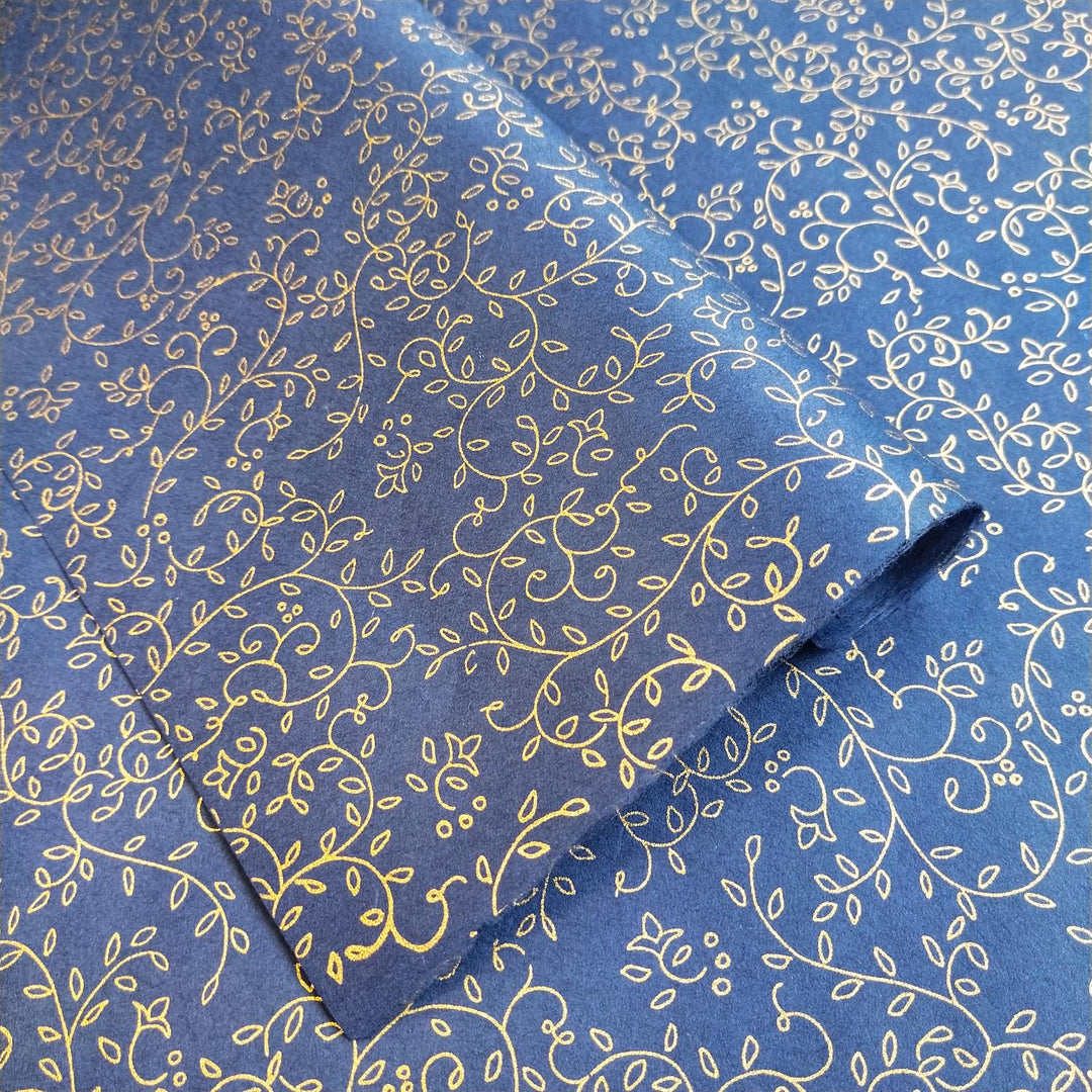 Close-up of blue screen-printed mulberry paper from Kozo Studio showcasing gold floral leaf and tendril patterns on delicate handmade paper with one sheet folded to reveal the seamless design.