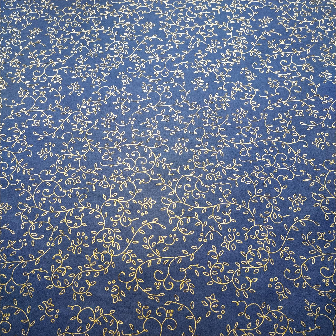 Handmade paper from Kozo Studio in a detailed view featuring grapevine-inspired gold motifs printed on blue mulberry paper with a folded edge highlighting its soft texture.