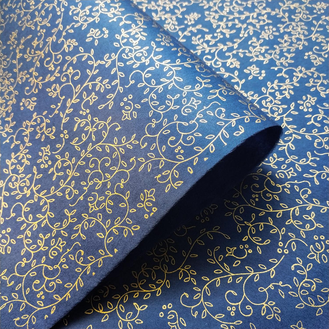 A high-resolution image of Kozo Studio mulberry paper in blue, screen-printed with elegant gold leaf and vine designs, folded to display the intricate handmade paper craftsmanship.
