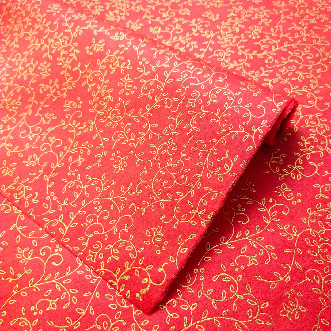 Red screen-printed mulberry paper from Kozo Studio featuring an intricate gold floral design with swirling vines and leaves, ideal for festive handmade paper projects.