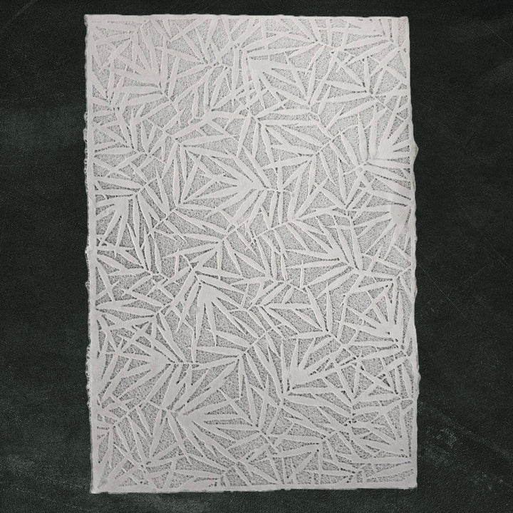 The Handmade Lace Kozo Paper (Bamboo) by Kozo Studio is a textured white mulberry paper with bamboo leaf pattern set against a dark green background.