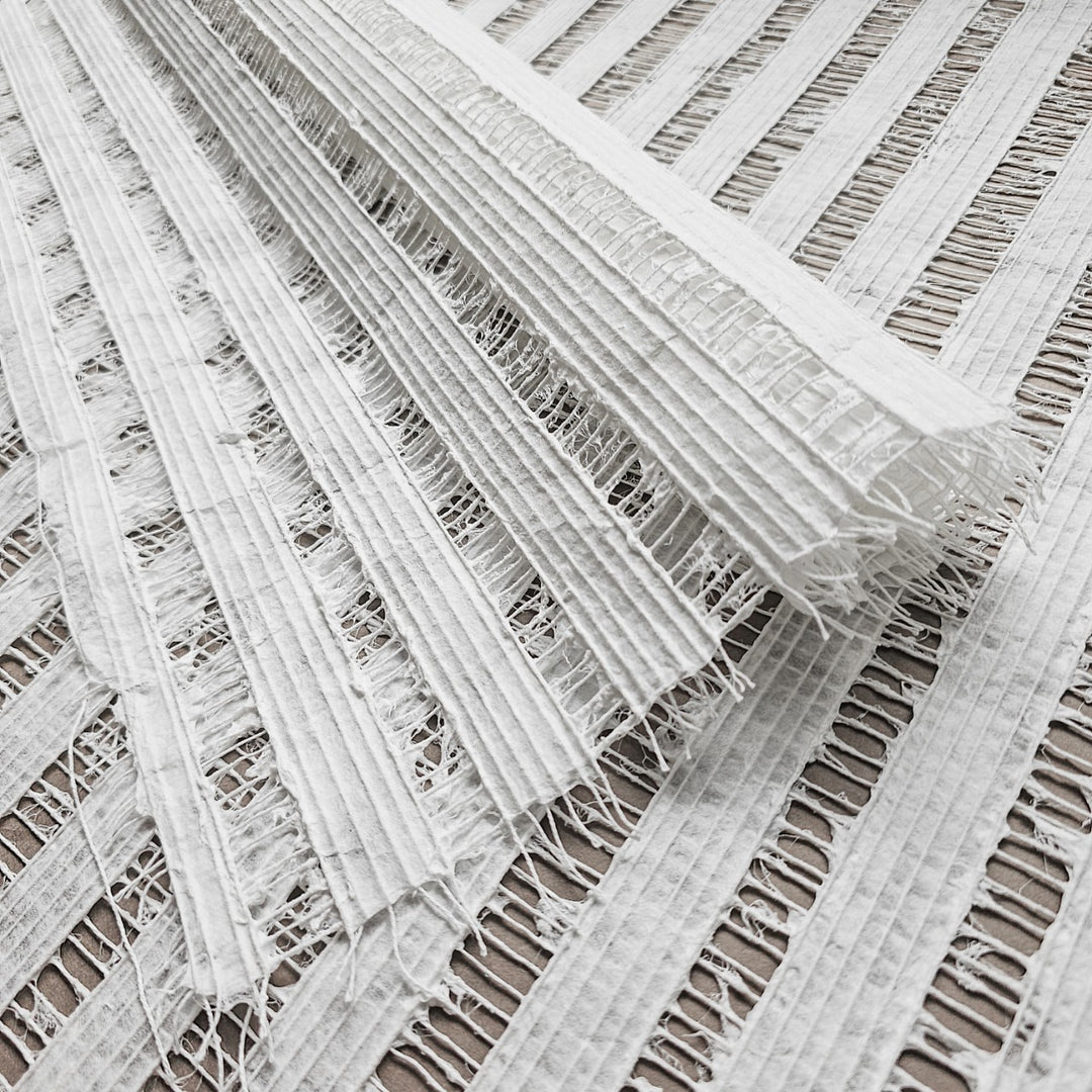 A close-up of the Handmade Geloma Kozo Paper (White) by Kozo Studio reveals its textured, layered beauty. The delicate weave and fringed edges resemble intricate rice paper, showcasing its fine frayed threads.