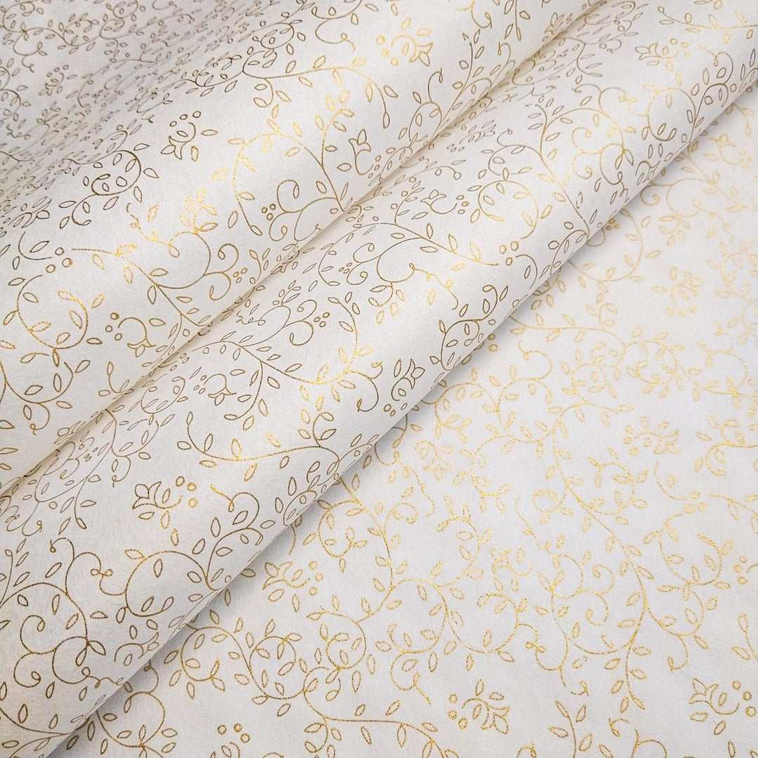 Close-up of Kozo Studio screen-printed handmade paper unrolled to show a refined gold floral pattern across white mulberry paper.