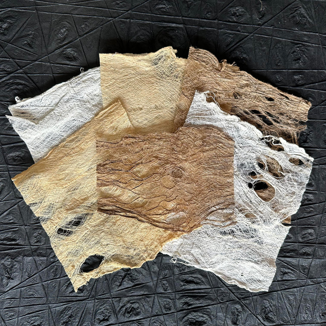 A collection of mulberry bark in white, beige, and brown with torn edges and holes is spread on a geometric-patterned black surface. Ideal for artistic creations, ranging from scrapbooking, collage, to 3D paper modeling.