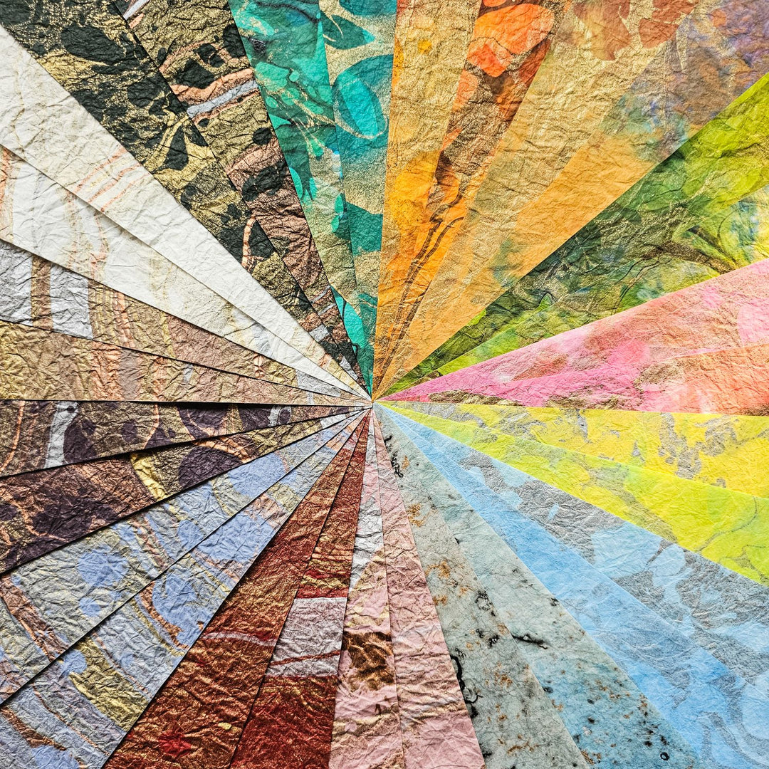 The A4 Milano Kozo Paper Pack by Kozo Studio features a vibrant fan-shaped display of 30 textured swatches, highlighting 15 designs. These include rice and mulberry paper in an array of colors and patterns, from bright yellows, greens, blues to earthy marbled and abstract designs.