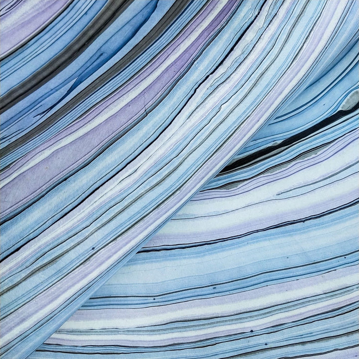 Artistic photograph of Kozo Studio mulberry paper with blue and purple diagonal marbling, ideal for handmade paper projects and decoration.