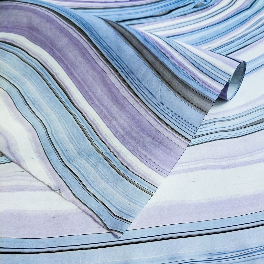 Close-up of marbled mulberry paper from Kozo Studio showing blue and purple waves in a handmade paper design, perfect for crafts and artistic use.