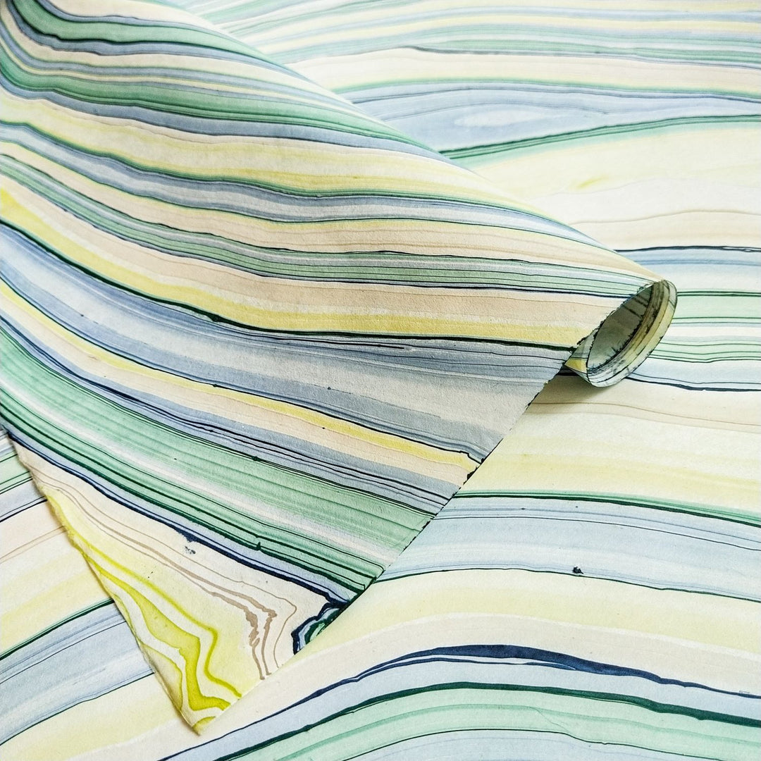 Close-up of handmade mulberry paper from Kozo Studio featuring Marble Design 3 with swirling patterns in yellow, green, blue, and cream. The textured kozo paper creates a sense of movement and artistic elegance.