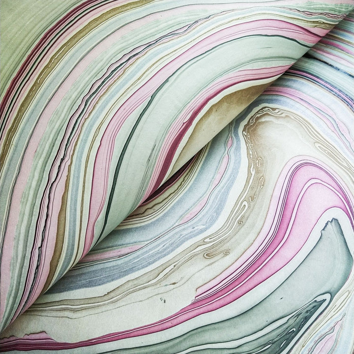 Close-up of an open book reveals Marble Kozo Paper by Kozo Studio, featuring swirling marbled pages in pastel pink, green, and beige. The dynamic abstract design resembles Mulberry Paper textures or natural stone.