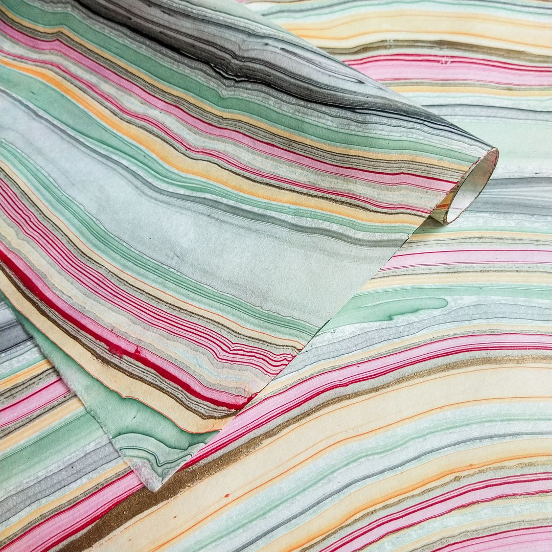 Close-up of handmade marble paper from Kozo Studio, featuring pastel swirls in pink, green, yellow, and gray on textured mulberry paper. Ideal for crafting and art projects.