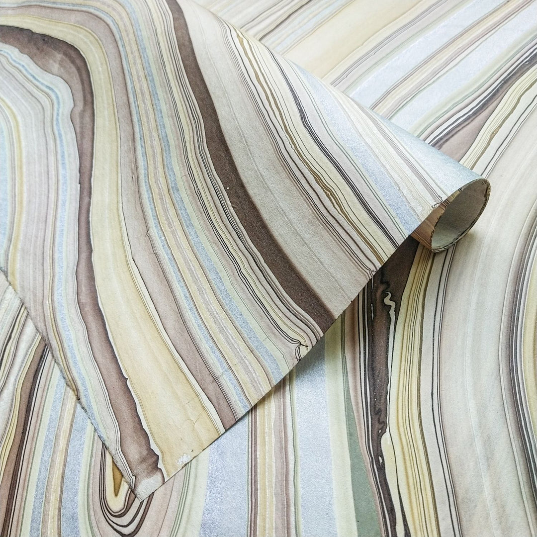 Marble Kozo handmade paper by Kozo Studio featuring earthy swirls of beige, silver, and brown, crafted from mulberry paper and partially rolled to reveal its natural texture.