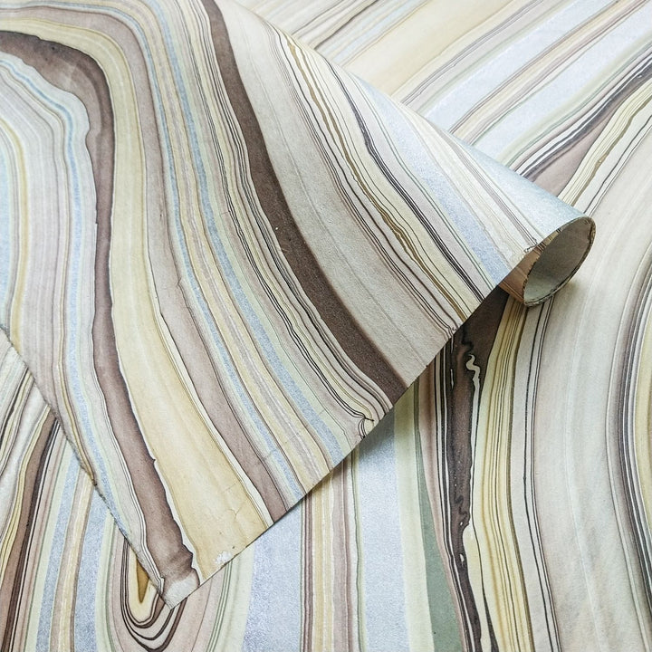 Marble Kozo handmade paper by Kozo Studio featuring earthy swirls of beige, silver, and brown, crafted from mulberry paper and partially rolled to reveal its natural texture.
